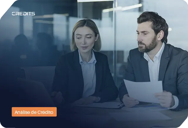 Dois profissionais (mulher e homem) analisando documentos e notebook sobre grupo econômico na análise de crédito.