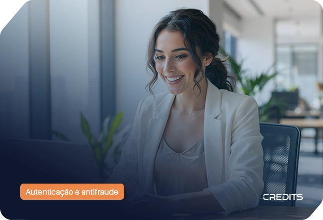 Mulher sorridente a usar computador em escritório com etiqueta 'Autenticação e antifraude' para onboarding digital B2B