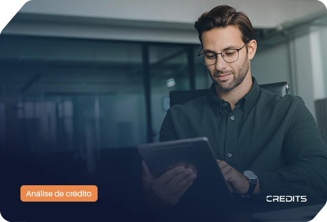 Homem de óculos a usar tablet em escritório com etiqueta 'Análise de crédito' para dossiê de crédito.